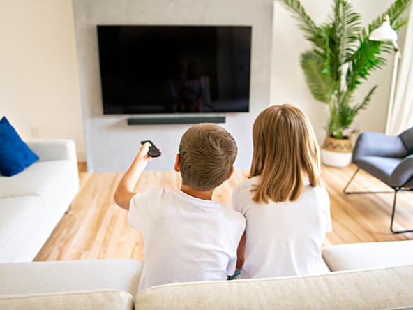back of the heads of a boy and girl watching TV, sitting on couch